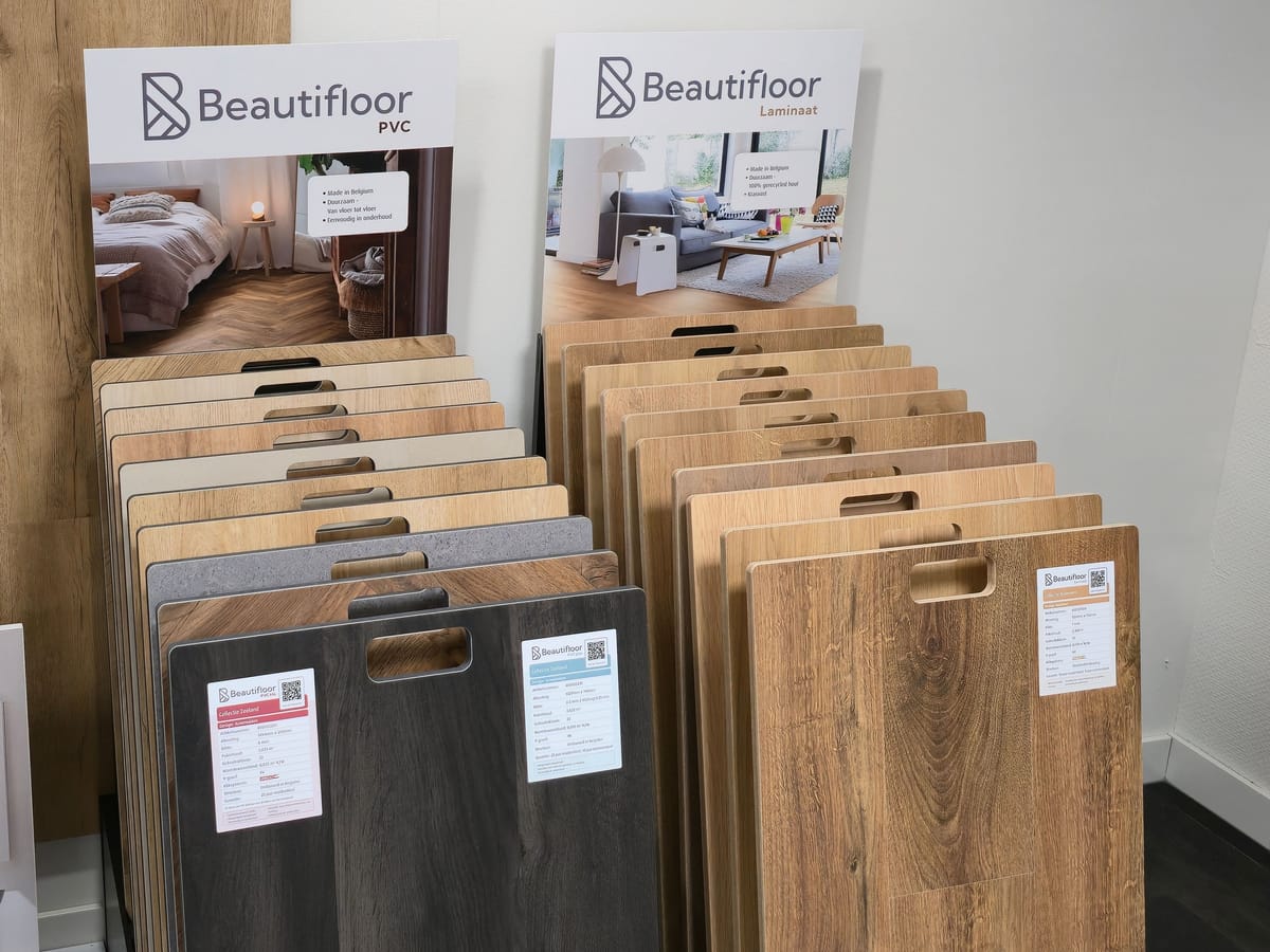 Twee rekken met vloerstalen van Beautifloor in de winkel, PVC links en laminaat rechts, met op elk rek een staalkaart