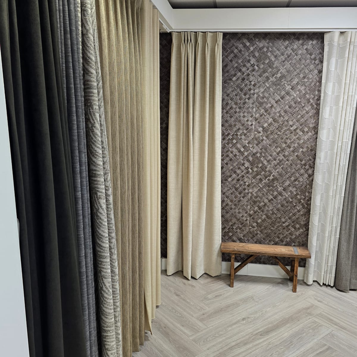 Gordijnen in verschillende stoffen en kleuren aan plafondrails in de showroom, met een houten bankje