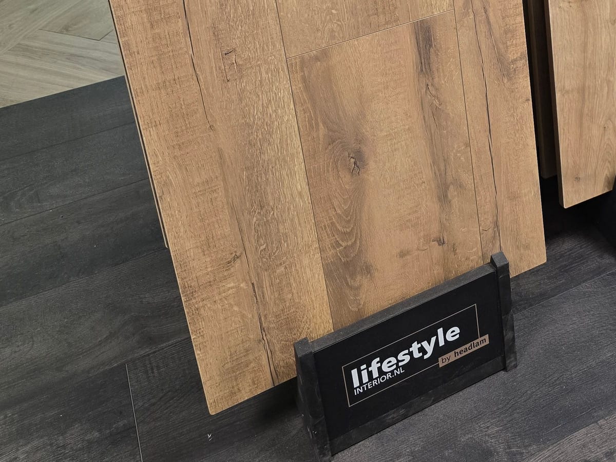 Een staal eikenlaminaat van Lifestyle Interior op de vloer van de winkel, met het bordje van het merk ervoor