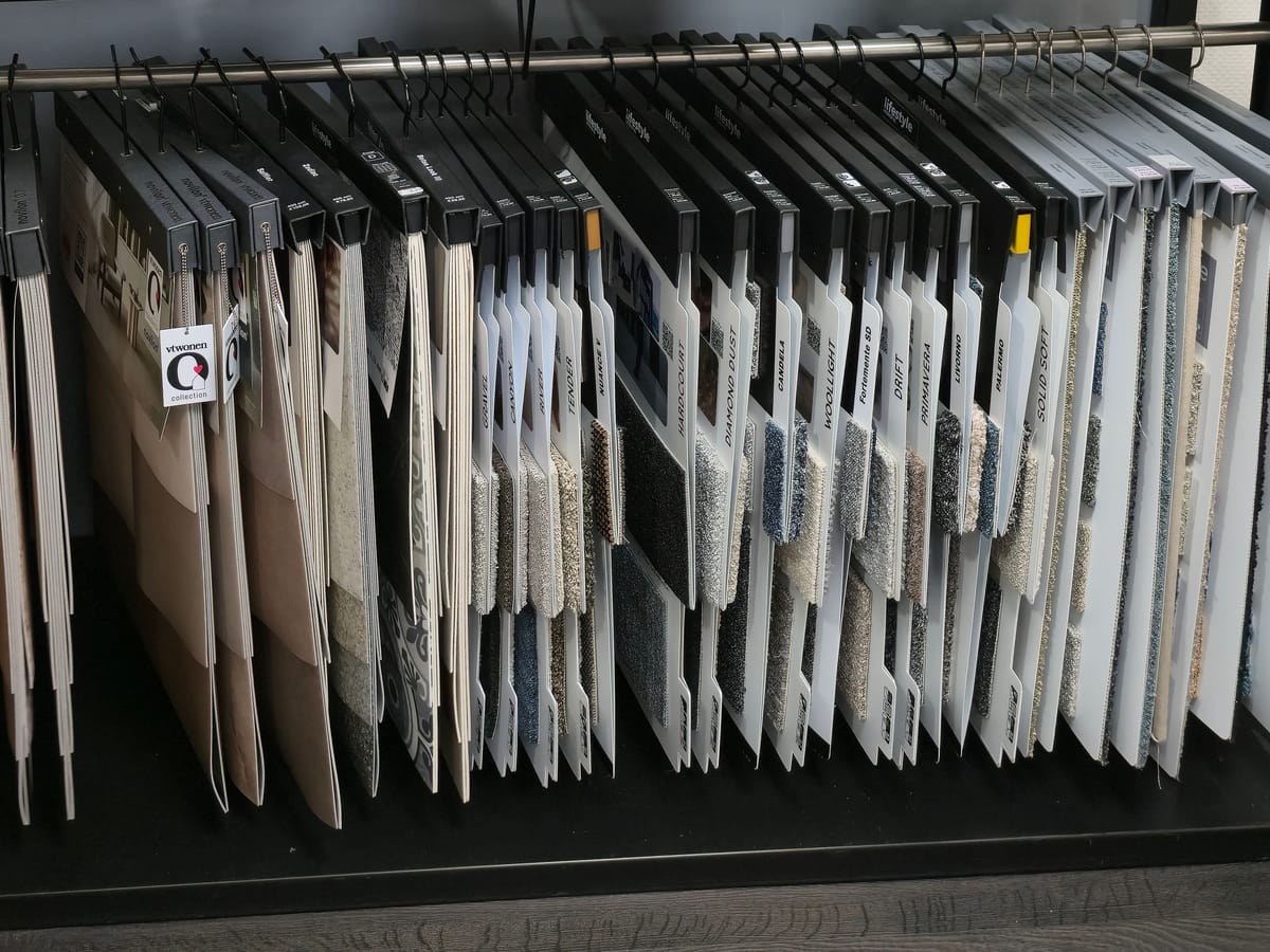 Een rek met tapijtstalen aan hangers in de winkel, in grijs, beige, wit en blauw