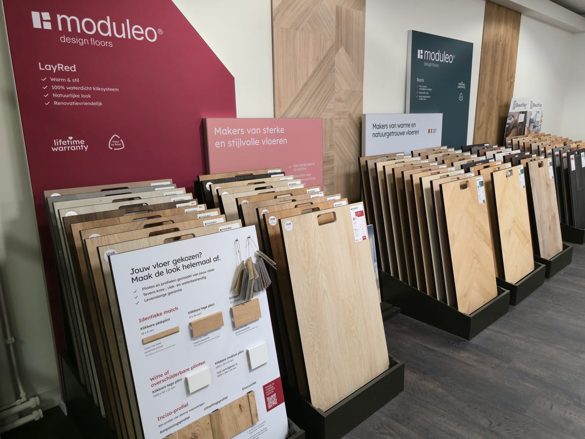 Rekken met pvc-stalen van Moduleo in de winkel, met een bord met bijpassende plinten en profielen