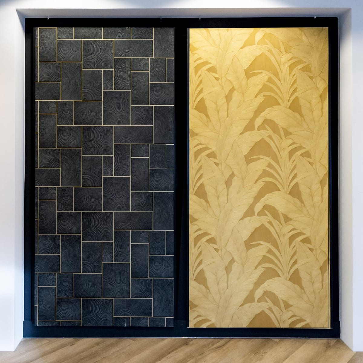 Twee behangpanelen in de showroom: een donker geometrisch dessin en een gouden palmbladdessin