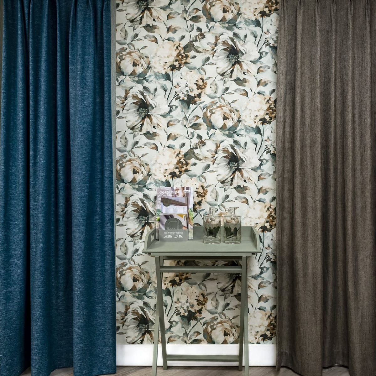 Een blauw en een bruin overgordijn aan weerszijden van een wand met bloemenbehang