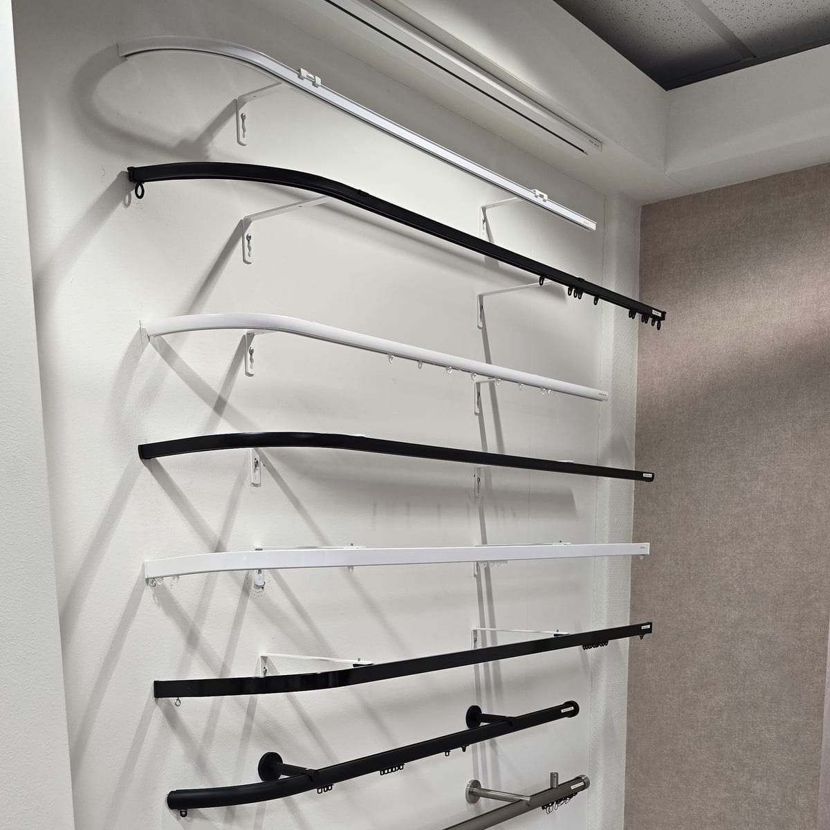 Witte en zwarte gordijnrails met gebogen uiteinden aan een wand in de showroom