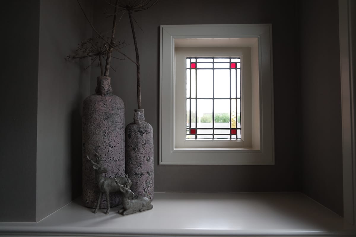 Grijs gestuukte wand met een klein raam met glas-in-lood en twee stenen vazen, uit het fotoalbum van Pro Finish