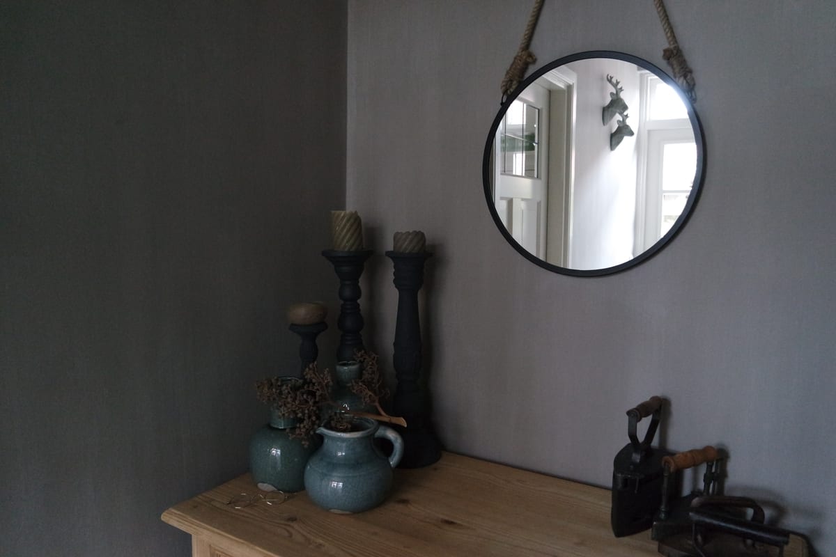 Grijs gestuukte wand met een ronde spiegel, kandelaars en kannen op een houten kast, uit het fotoalbum van Pro Finish