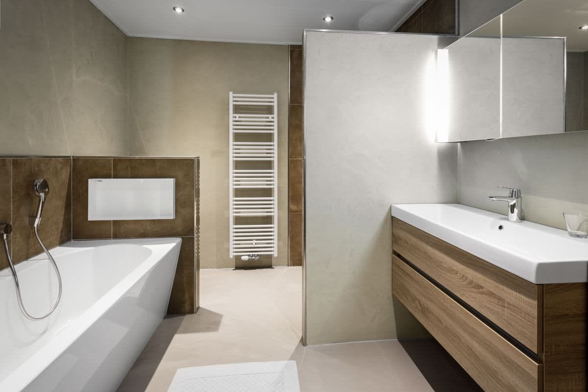 Badkamer met ligbad, wastafelmeubel en een lichte gestuukte wand