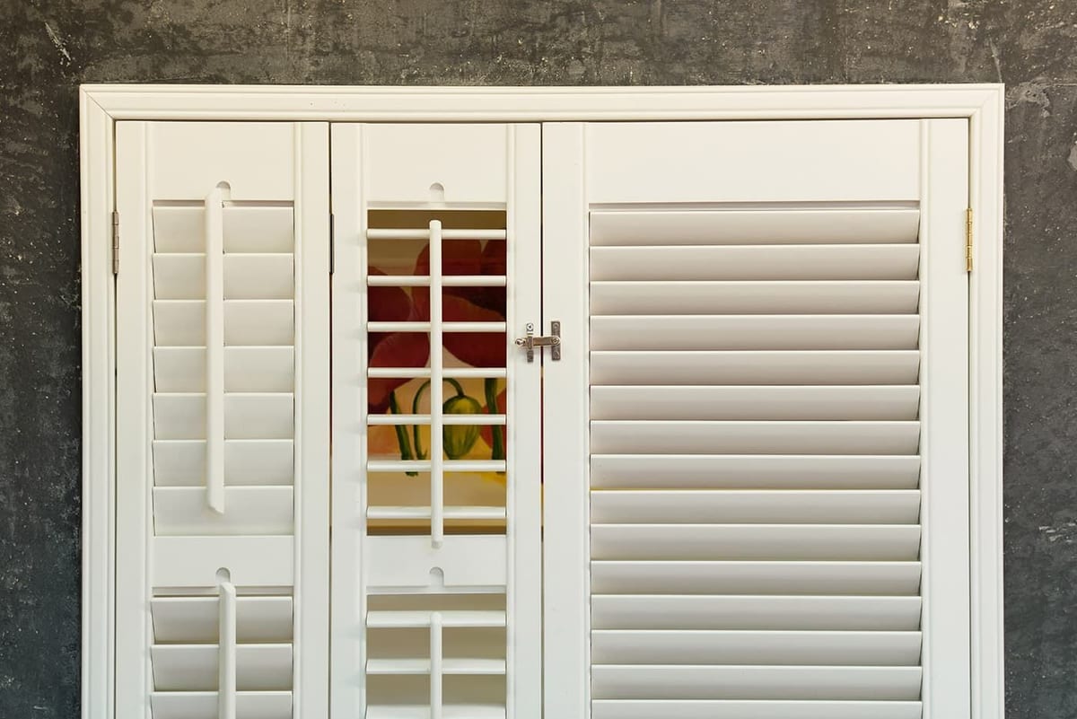 Witte shutters met verstelbare lamellen in een kozijn
