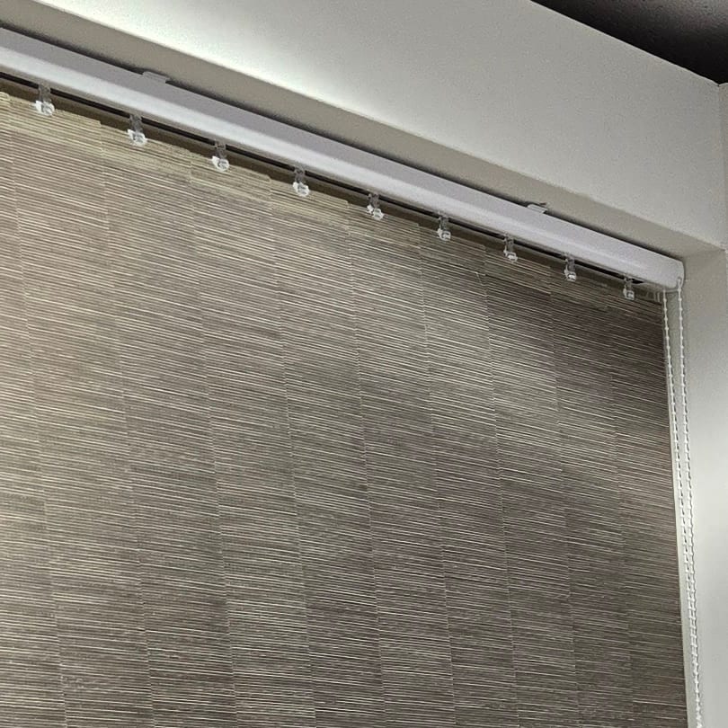 Verticale lamellen in een grijsbruine stof aan een witte rail, in de showroom
