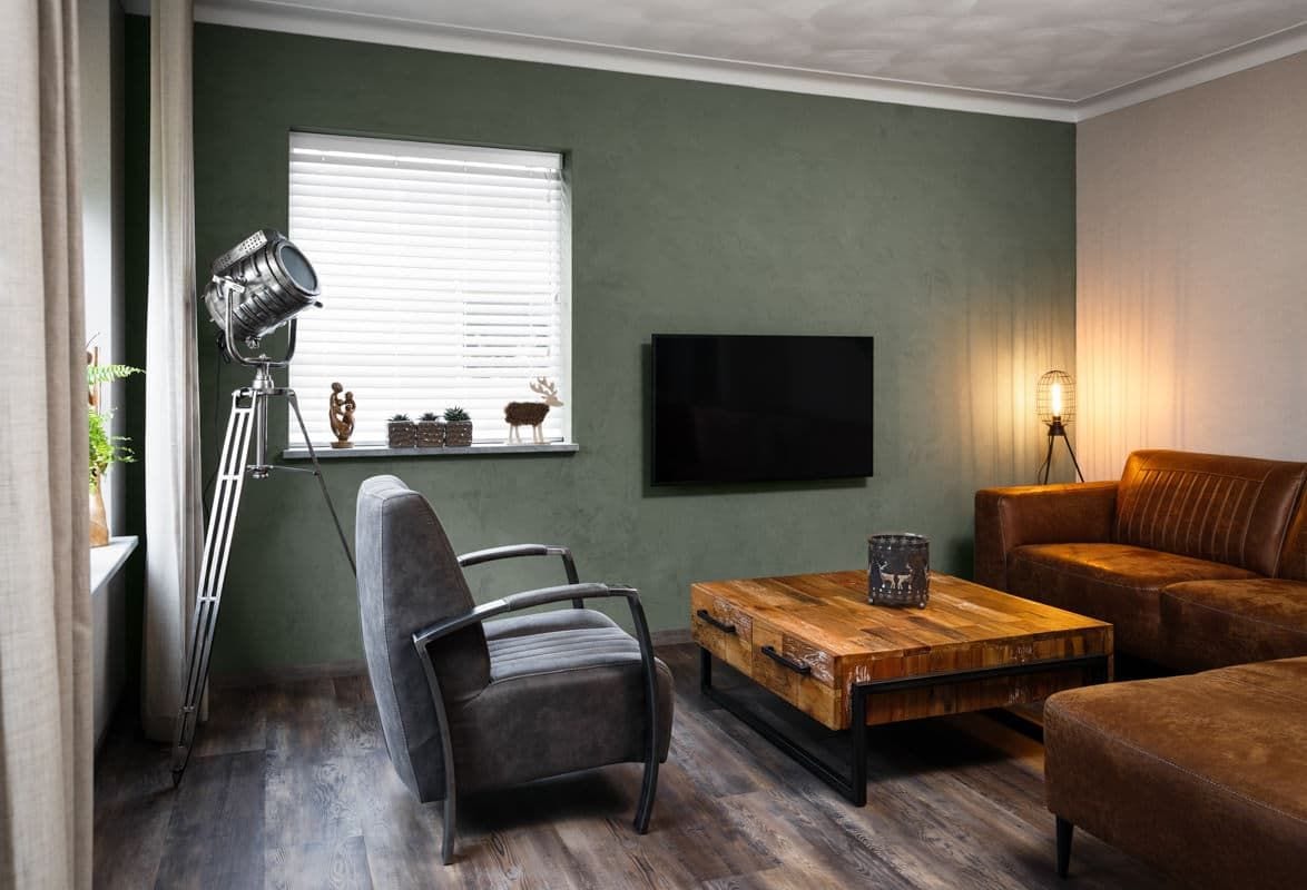 Woonkamer met een groen gestuukte wand, een leren bank en een stoere salontafel