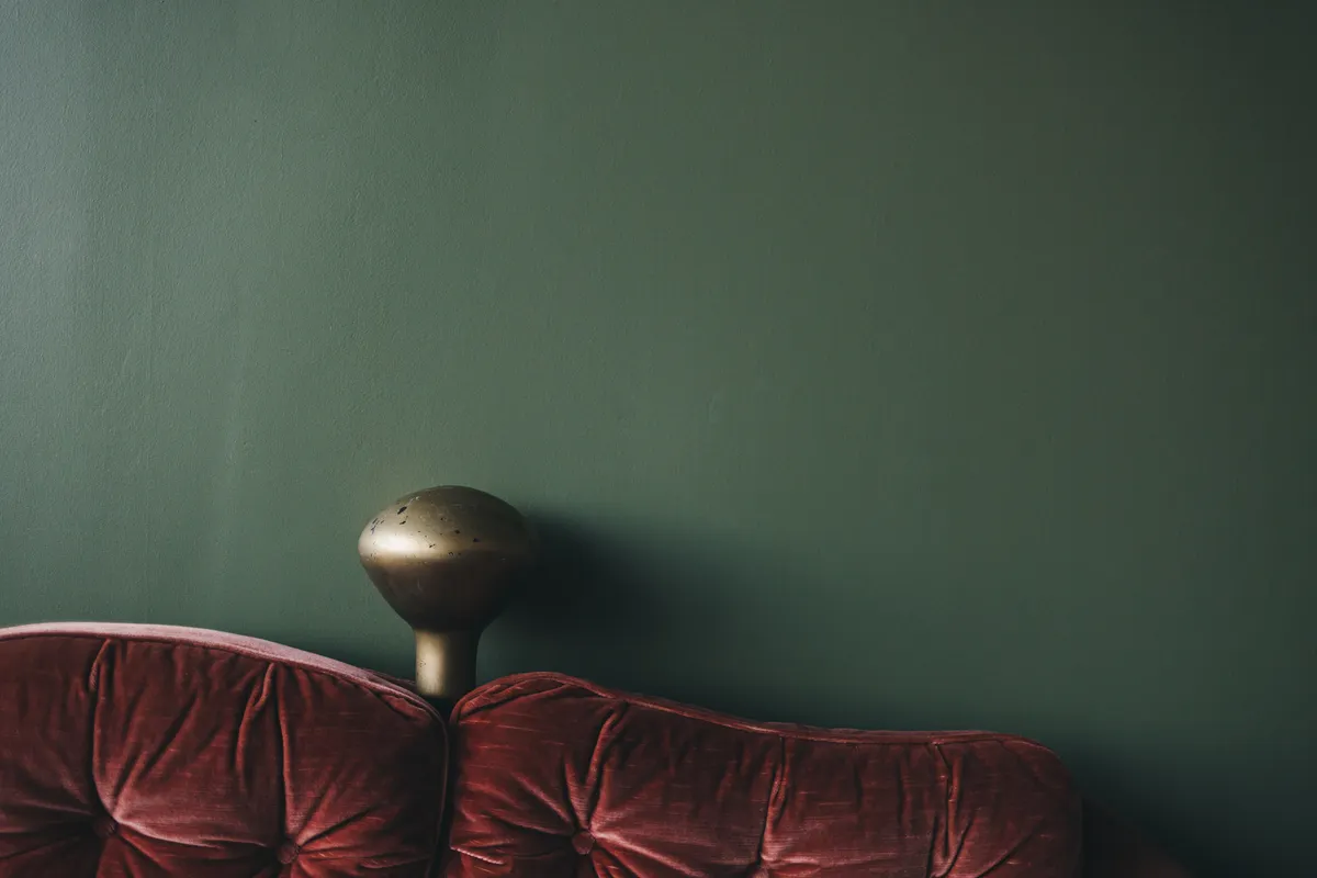 Velours bank voor een donkergroene wand met een lamp